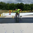 White house with black roof, chimney, and trim, blue sky, and green foliage.