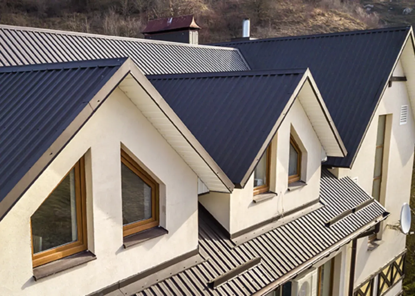 White house with black roof, chimney, and trim, blue sky, and green foliage.