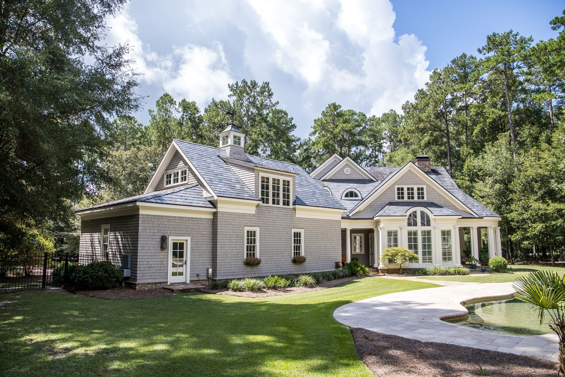 Elegant two-story house with gray siding, blue roof, surrounded by green trees and a curved driveway.