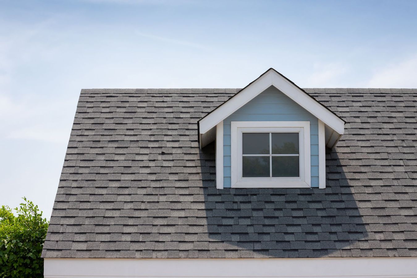 Gray asphalt shingle roof with a blue dormer and white trim, against a blue sky.