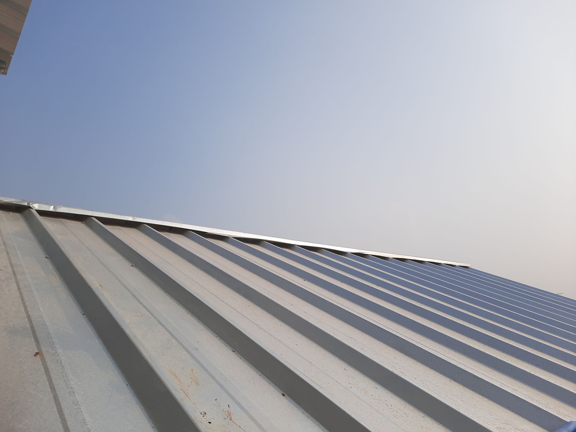 Metal roof with parallel ridges, set against a clear blue sky.