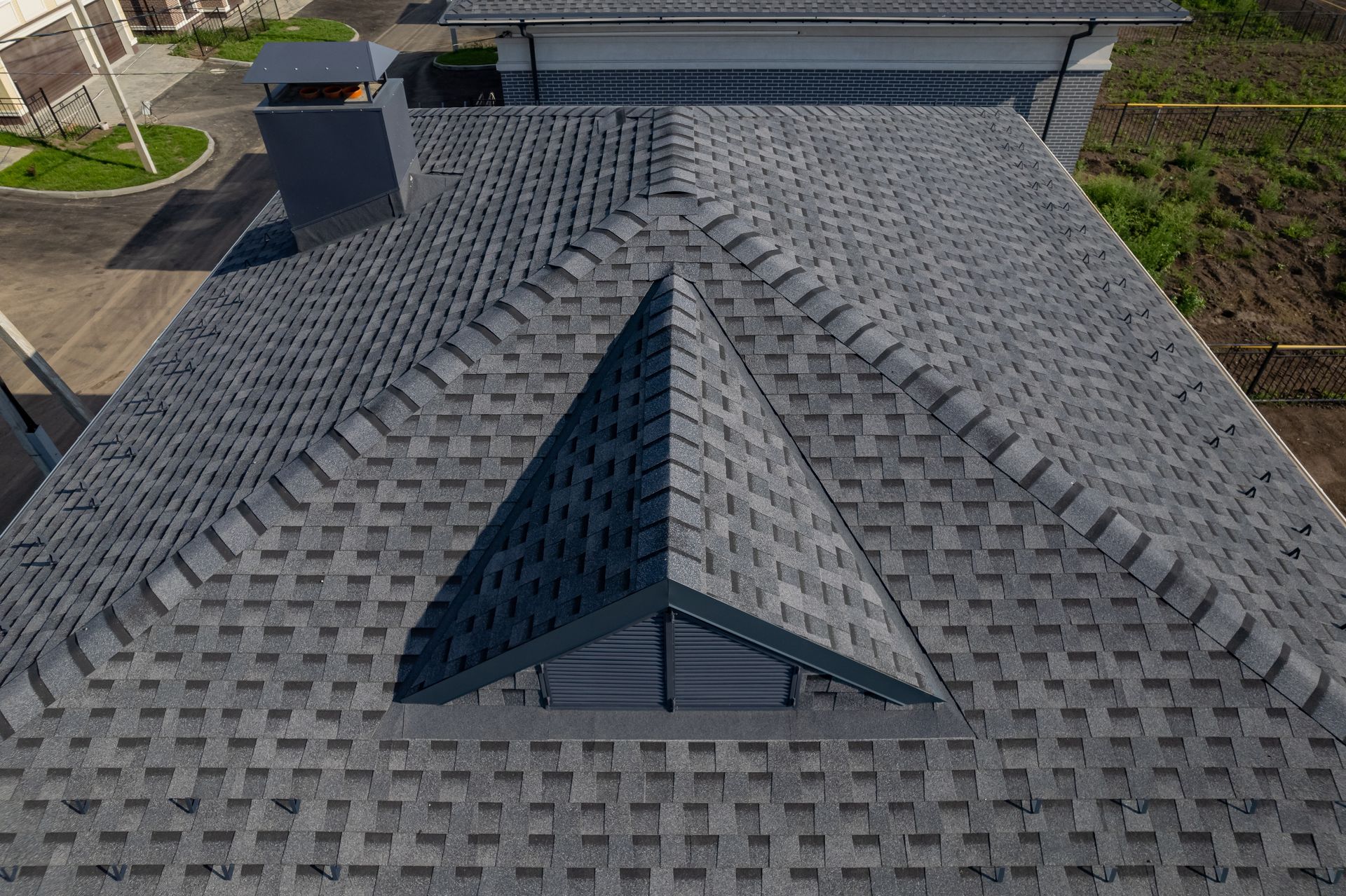 Overhead view of a house roof with dark gray shingles, including a triangular dormer and chimney.