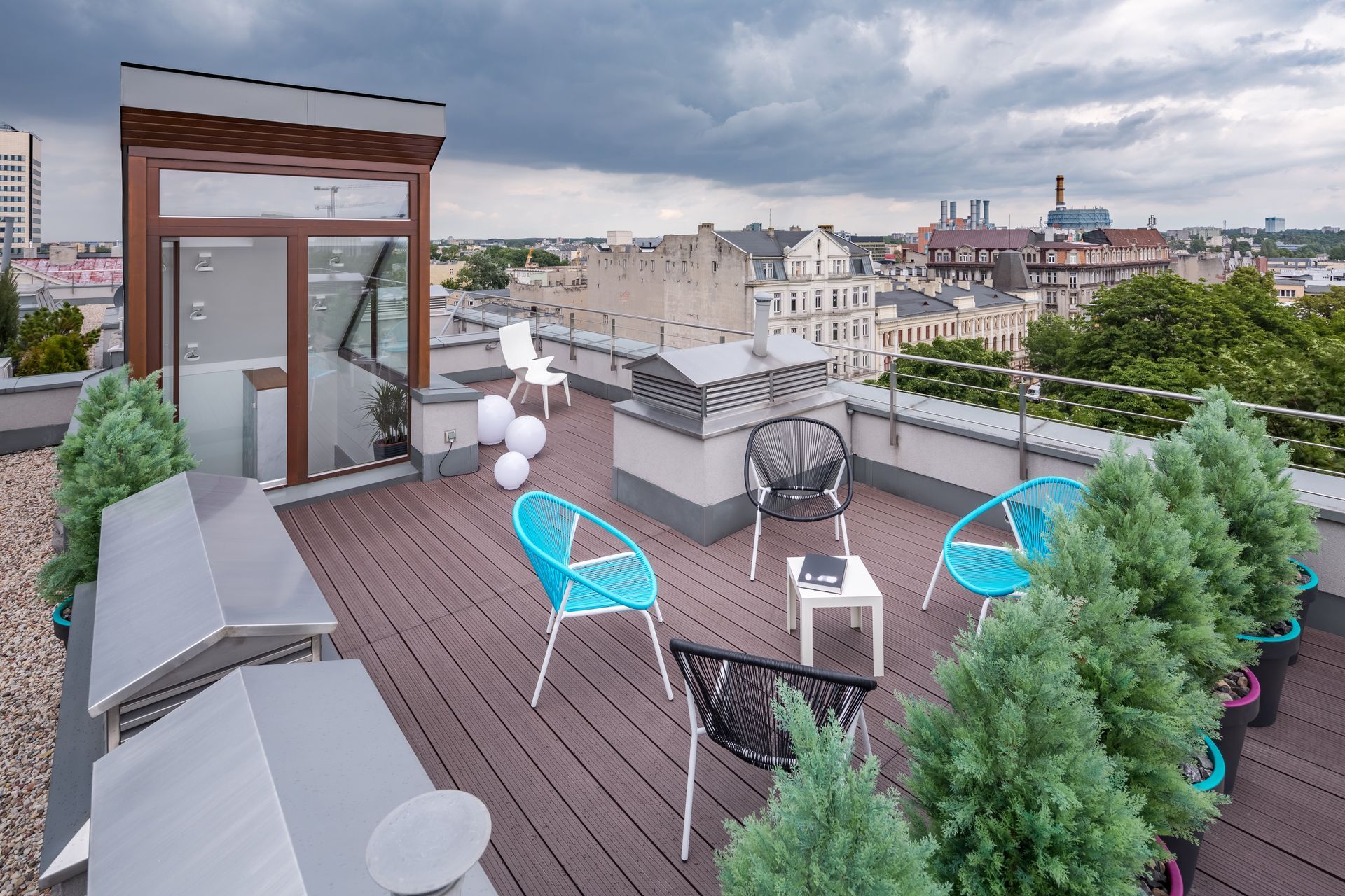Rooftop patio with blue chairs, small table, and greenery overlooking a city.