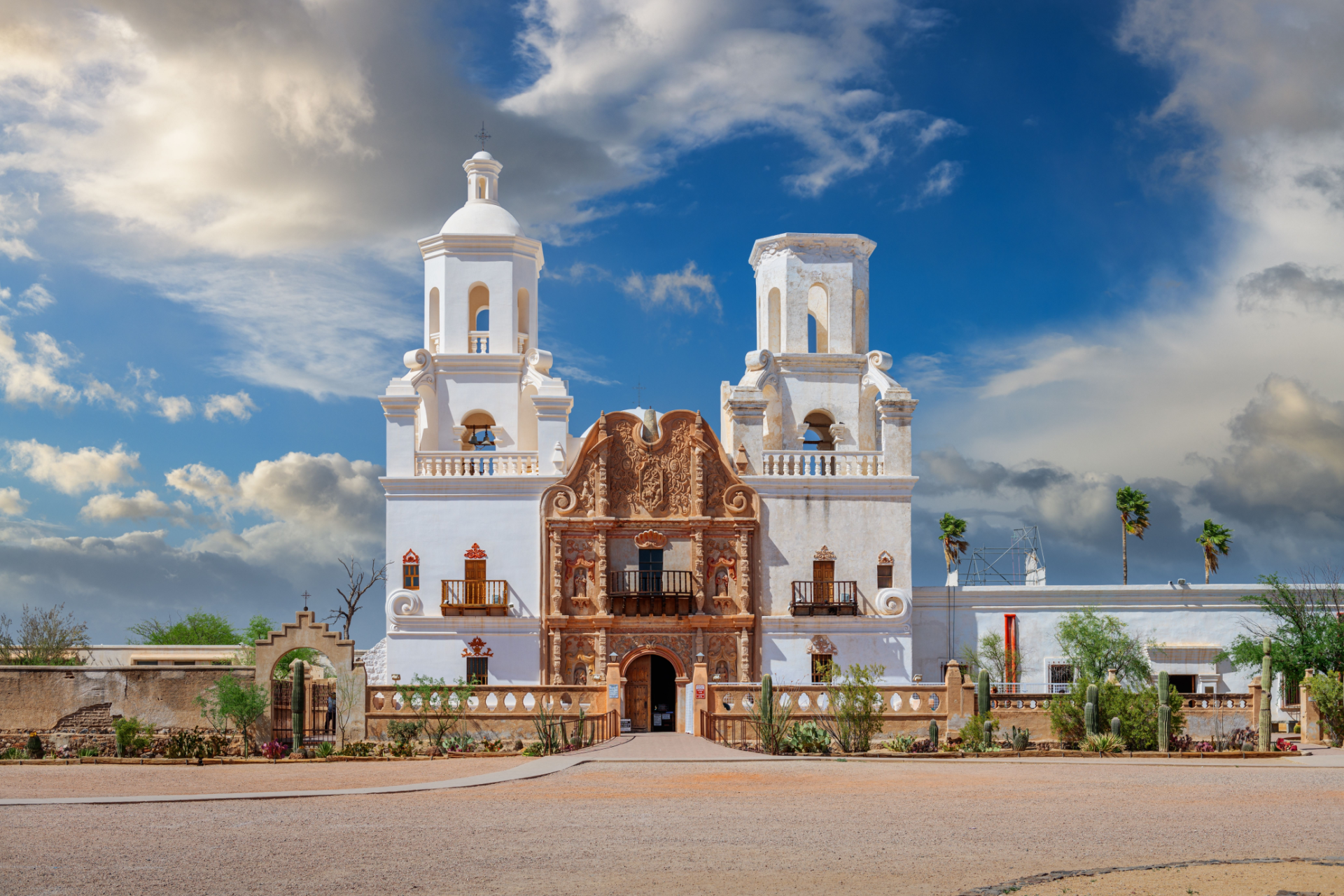 White mission church with two towers under a blue sky with clouds.