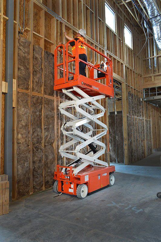 Un hombre está parado sobre un elevador de tijera en un edificio en construcción.