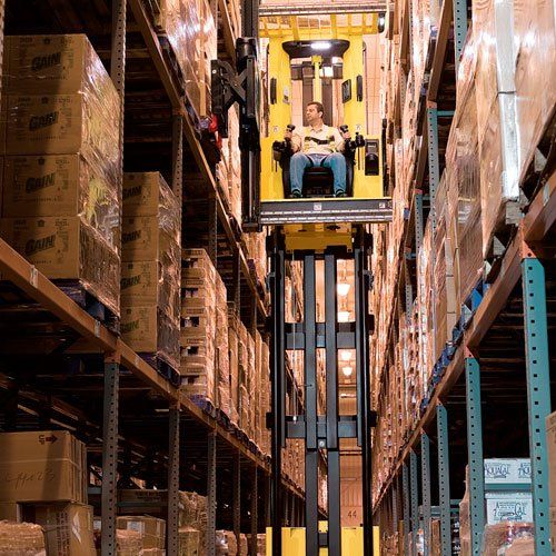 Un hombre monta una carretilla elevadora amarilla en un almacén.