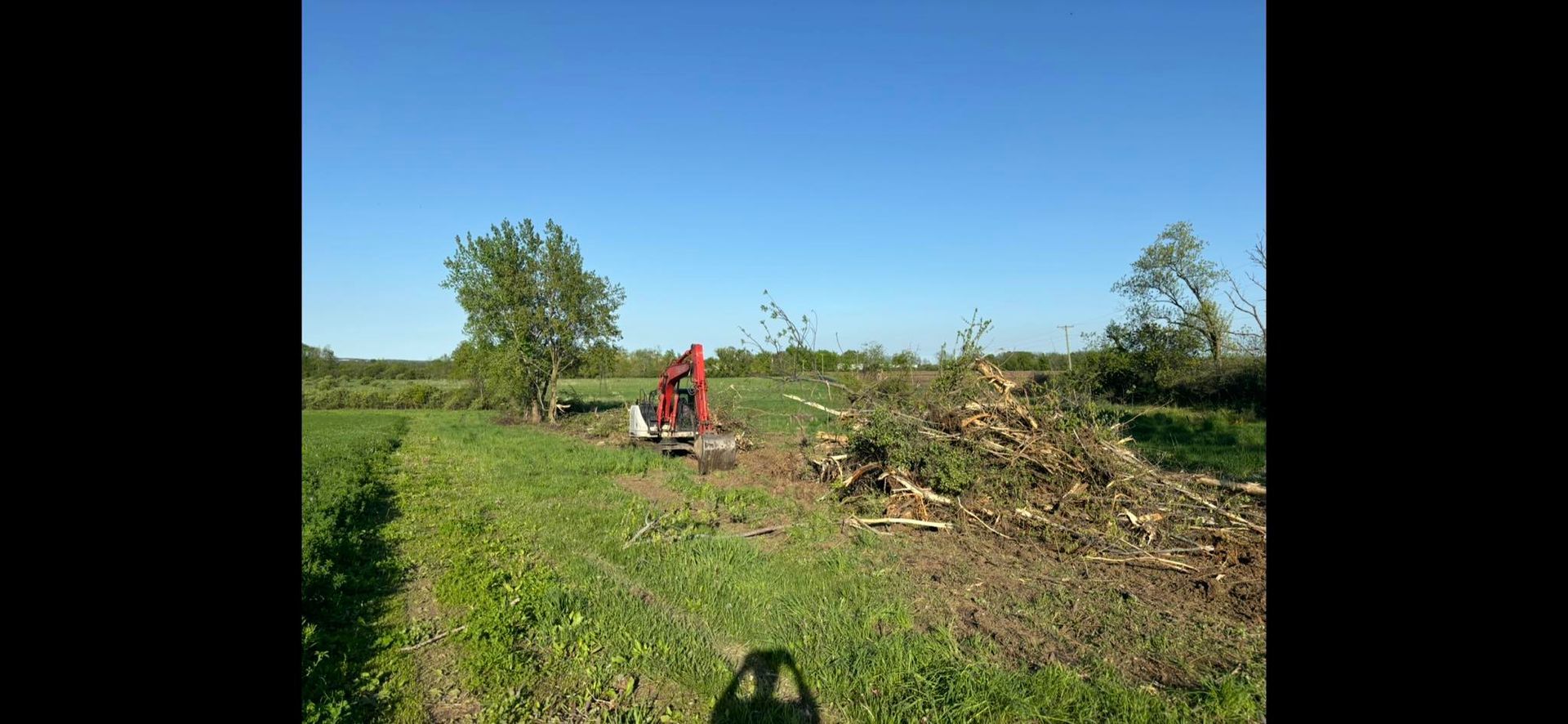 A red machine cutting branches in a field on a sunny day.