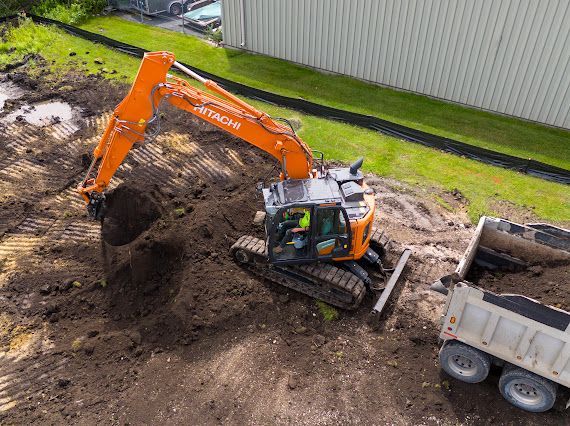 Orange Hitachi excavator loading a dump truck with dirt at a construction site.