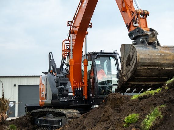 Orange excavator digging into a pile of dirt, working outdoors.
