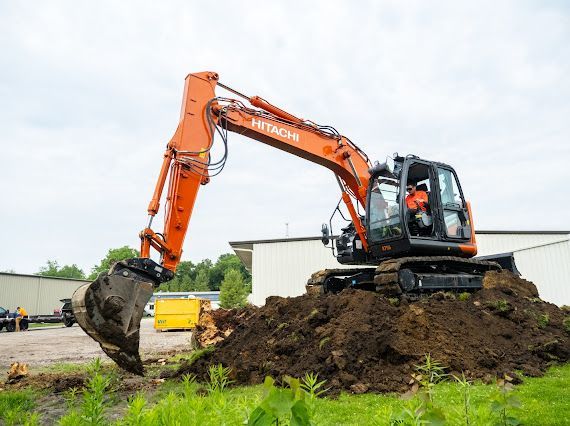 Orange Hitachi excavator digging in a dirt pile, overcast day.