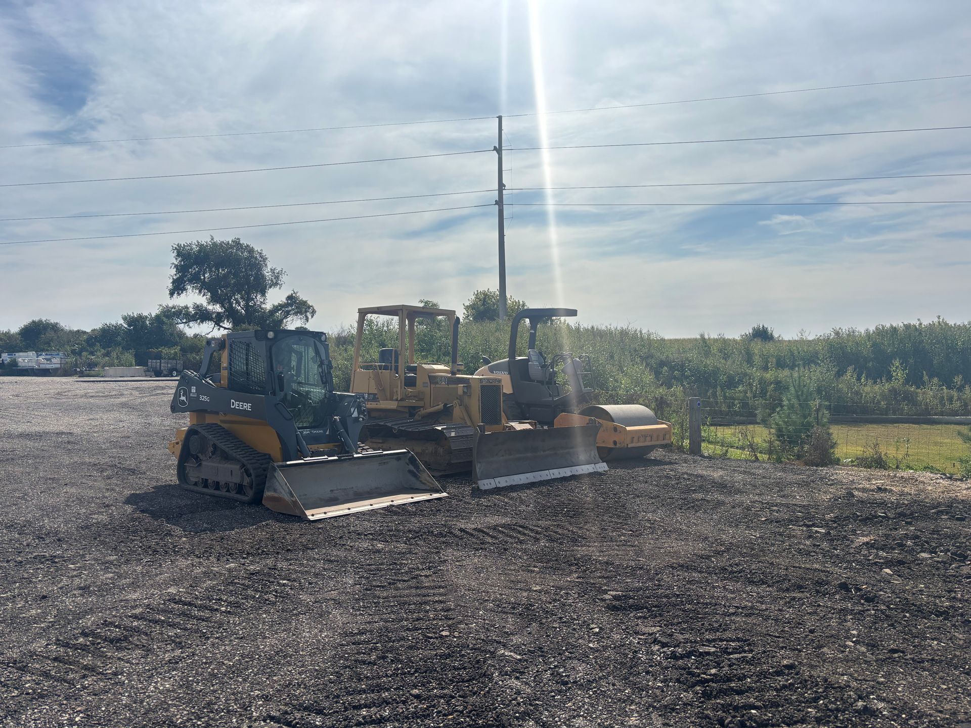 Three pieces of heavy machinery parked outdoors on gravel under a sunny sky.