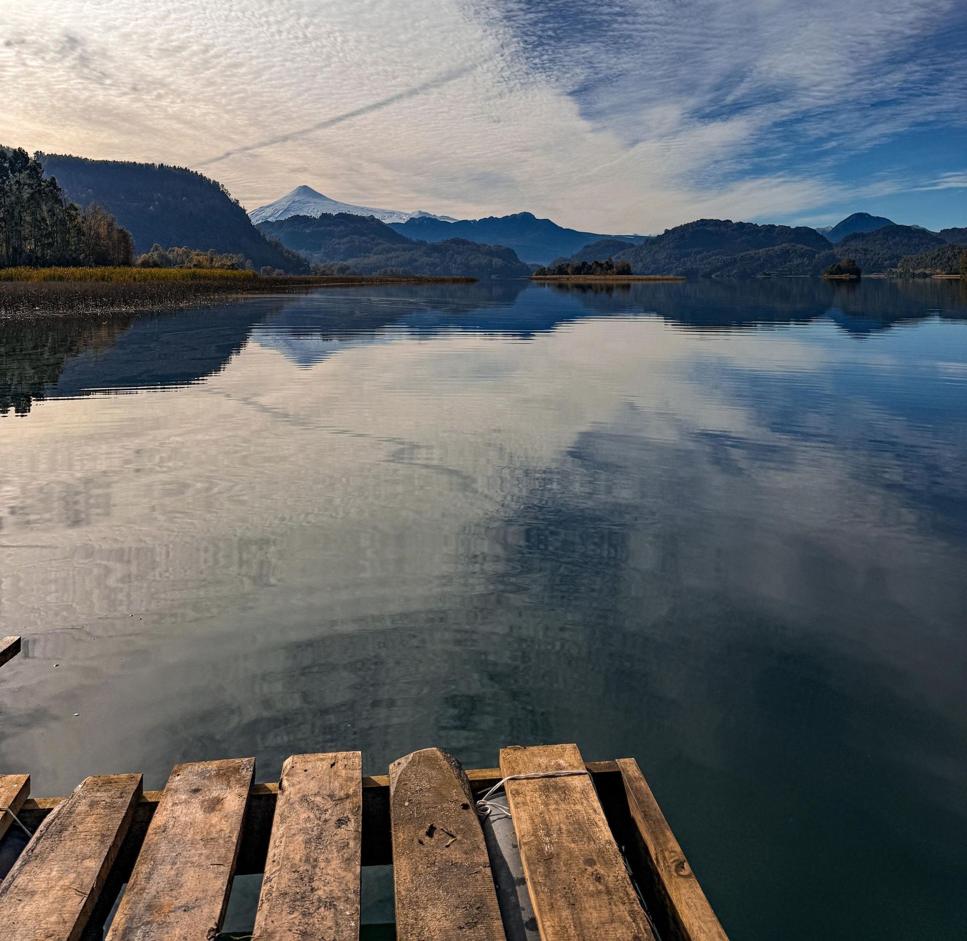 Un muelle de madera con vistas a un lago con montañas al fondo.