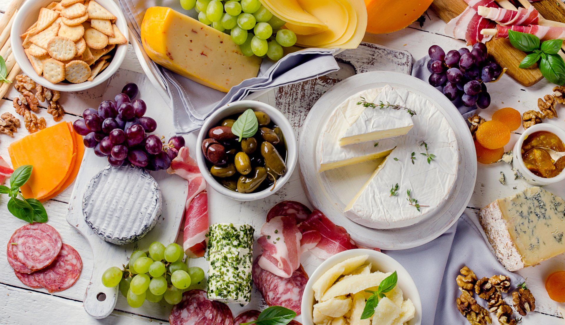 Charcuterie assortment, cheeses, olives and fruits on a white wooden background.