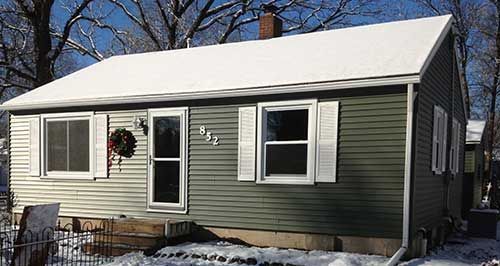 A small house with a wreath on the front door is covered in snow.