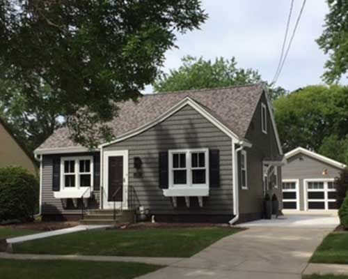 A small house with a gray siding and white shutters