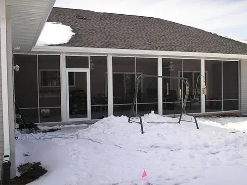 A house with a screened in porch and a swing set in the snow.