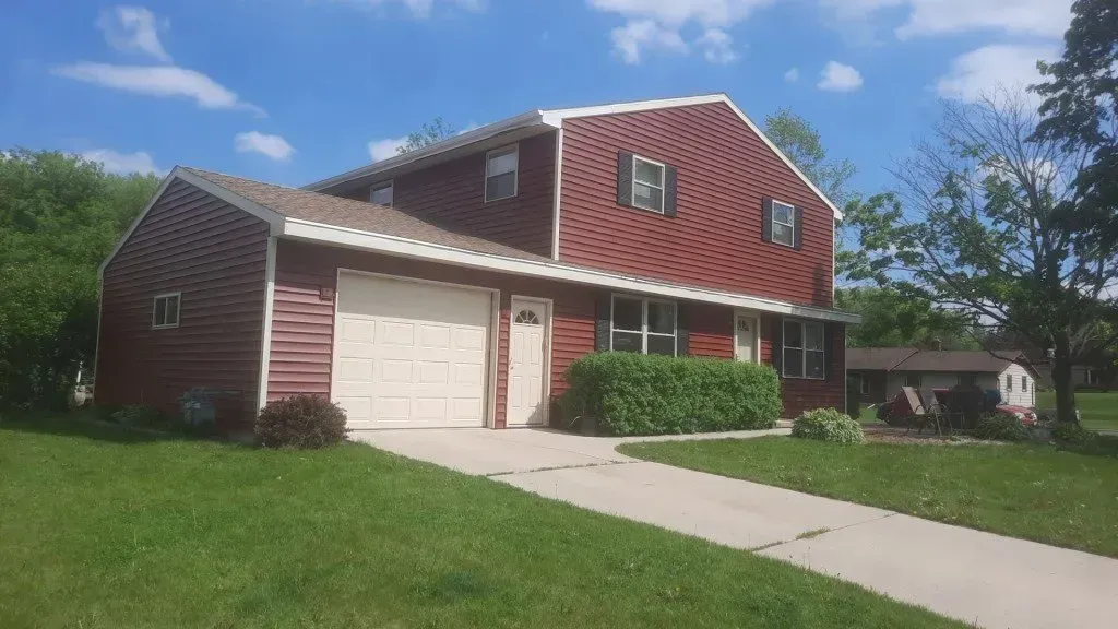 A red house with a white garage door is sitting on top of a lush green lawn.