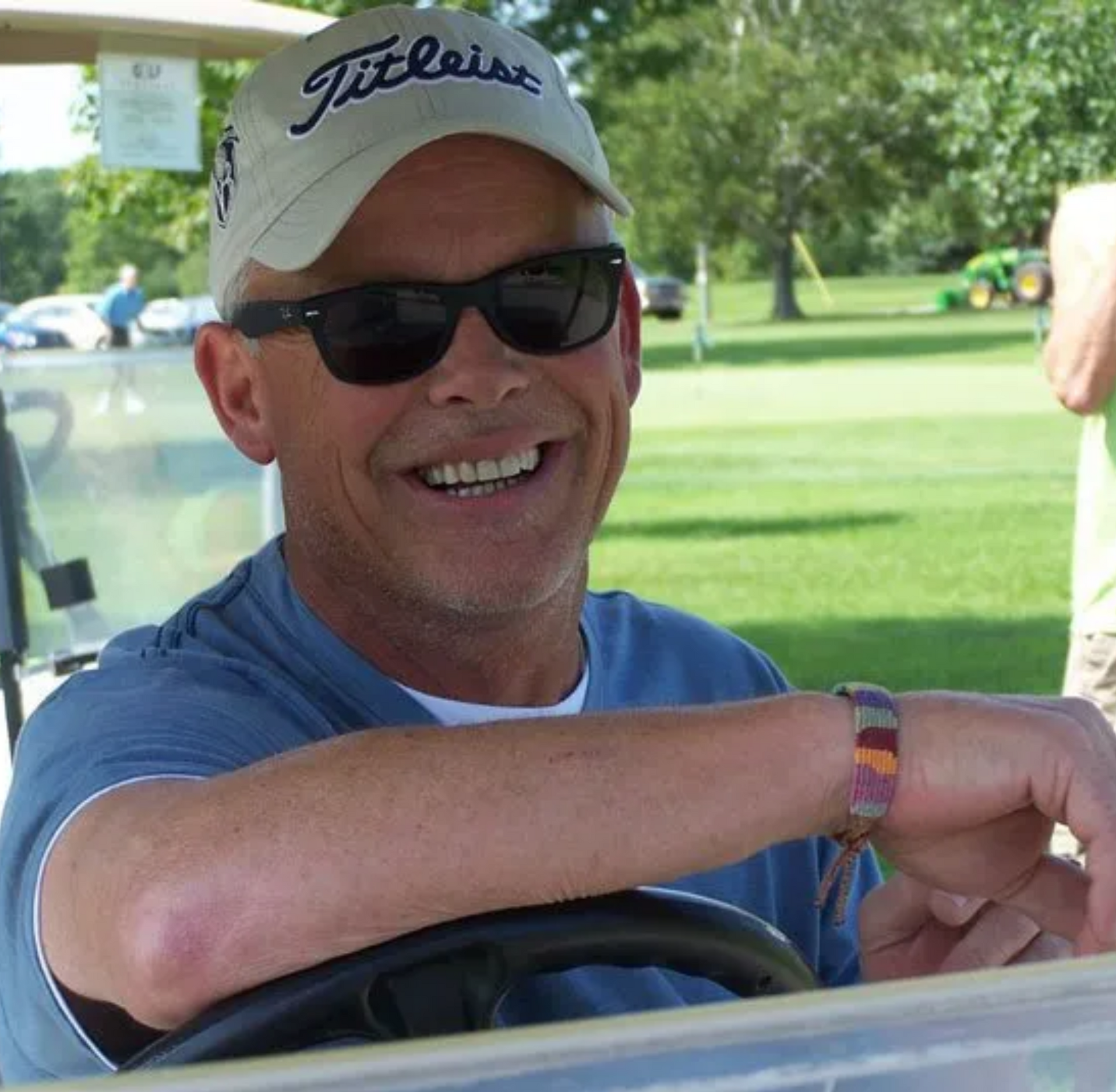 Owner wearing a titleist hat and sunglasses is sitting in a golf cart