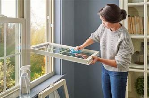 A woman is cleaning a window with a cloth in a living room.