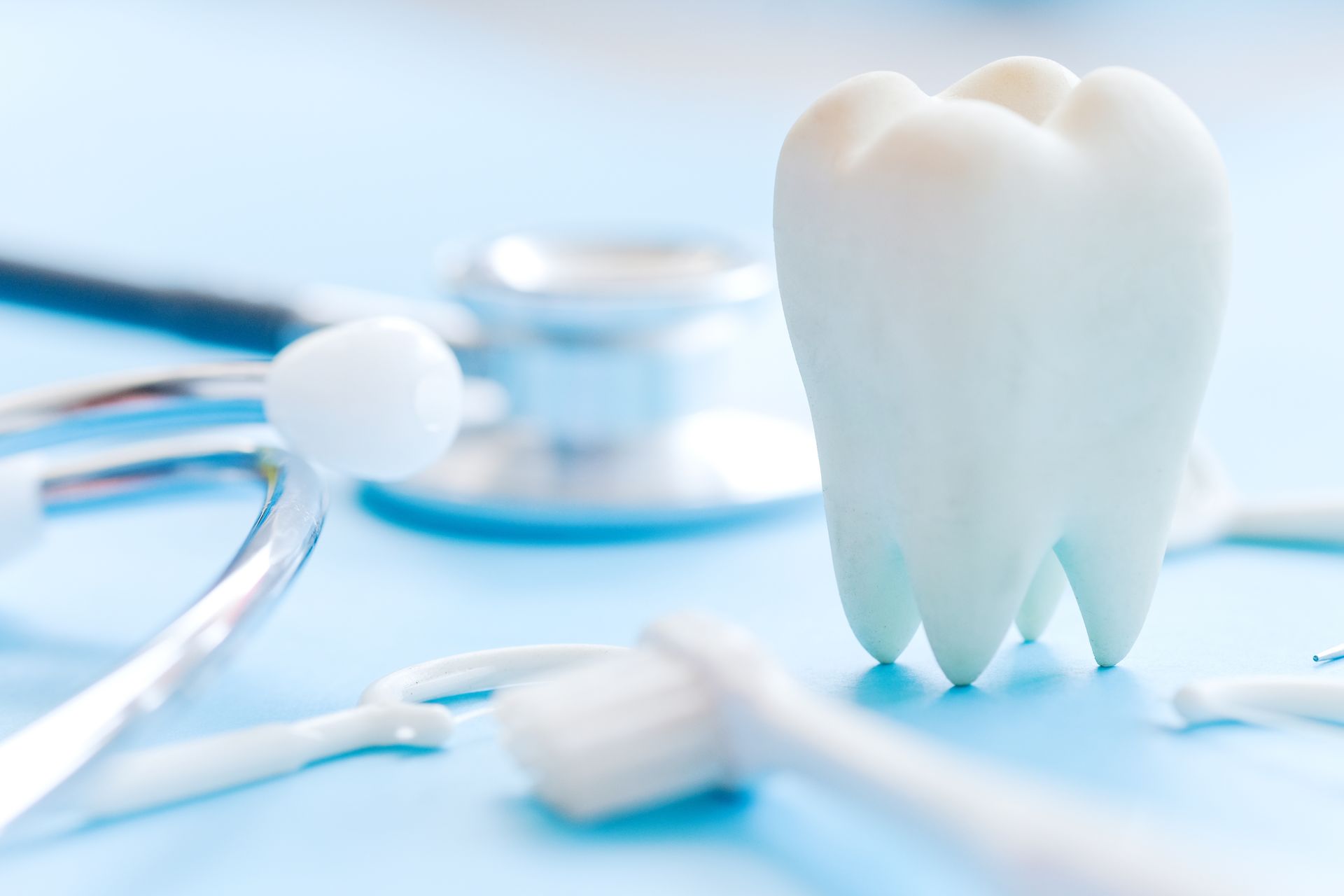 Dental tools beside a white molar tooth model on a blue background.