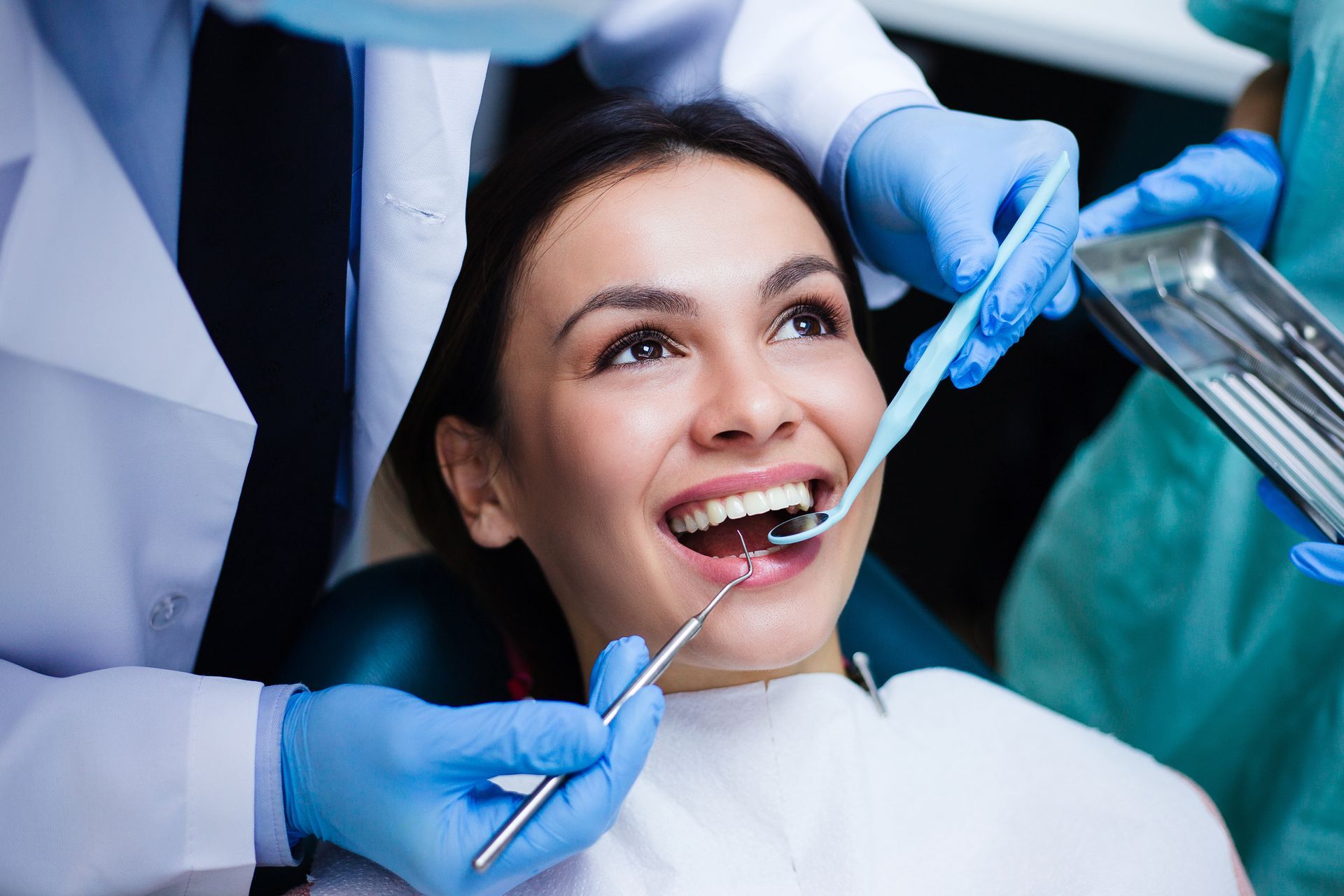 Dentist examining a smiling patient’s teeth with a mirror and probe in a clinic.