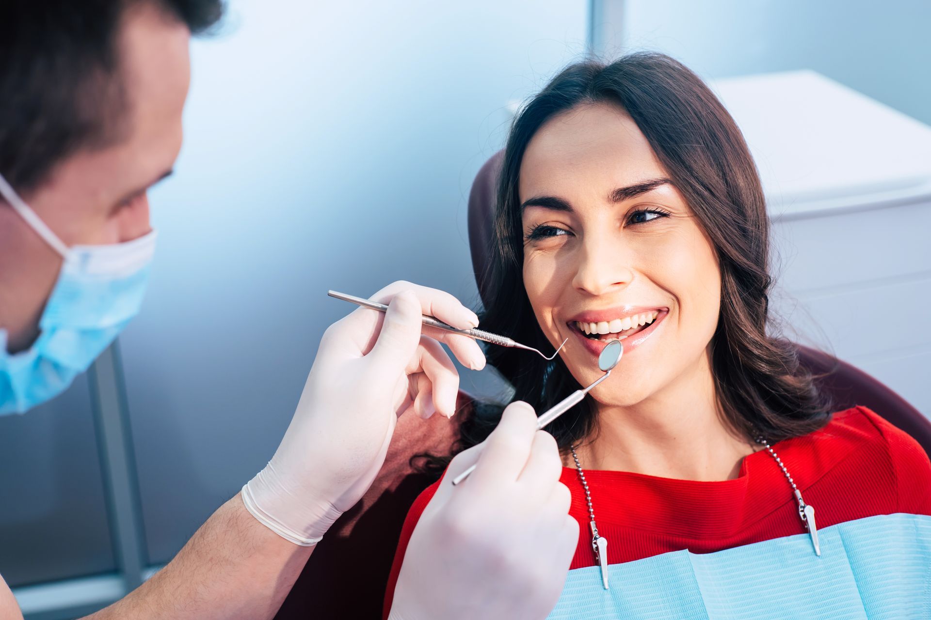 Dentist examining a smiling patient with dental tools in a clinic, wearing gloves and a mask.