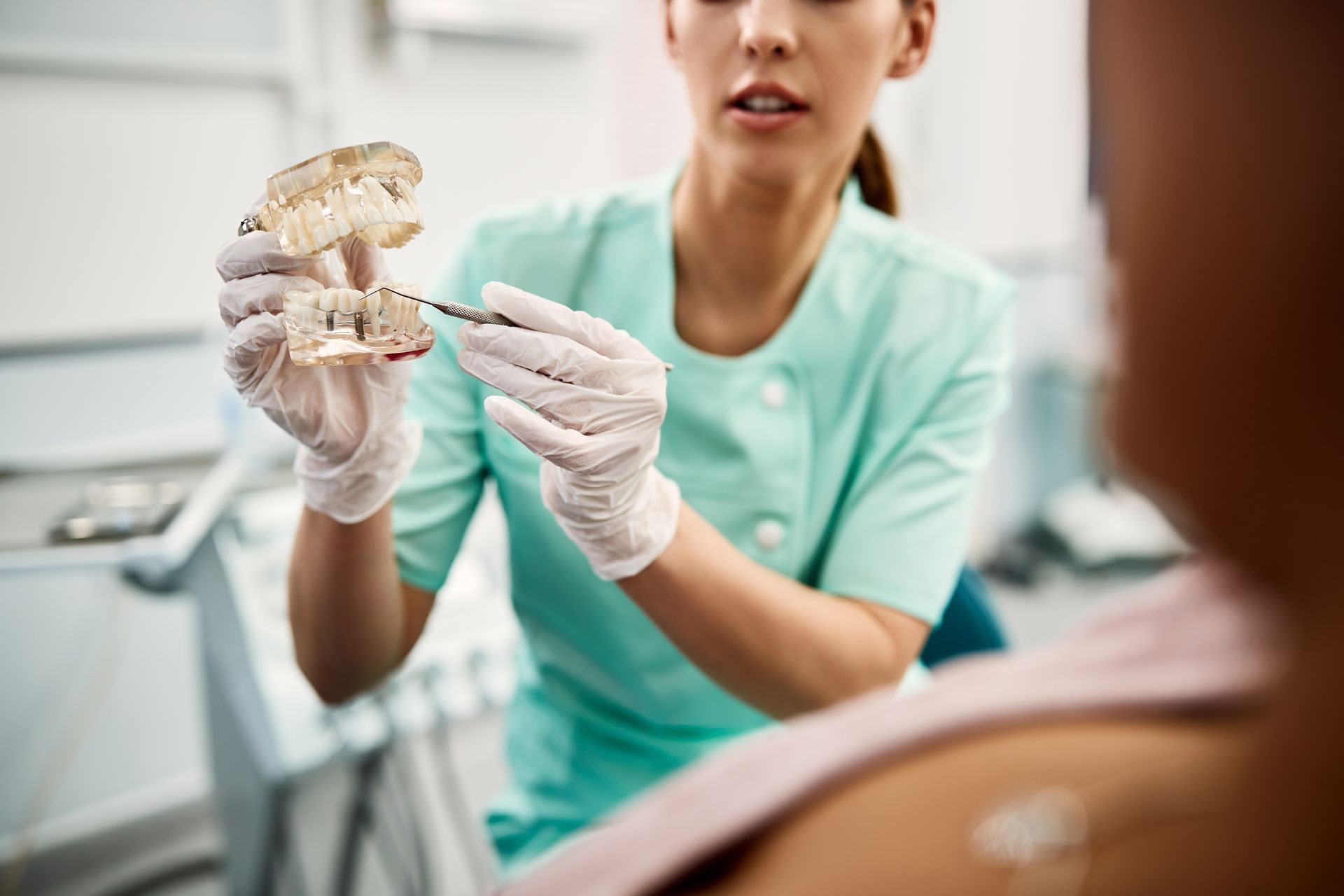 Dentist showing a dental mold to a patient in a clinic, wearing gloves and mint scrubs.