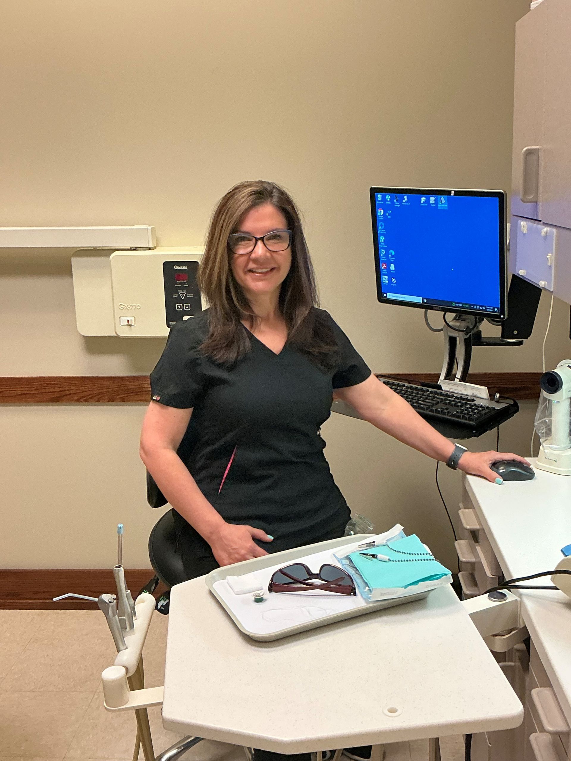 Woman standing beside a medical exam table in a clinic, next to a computer monitor.