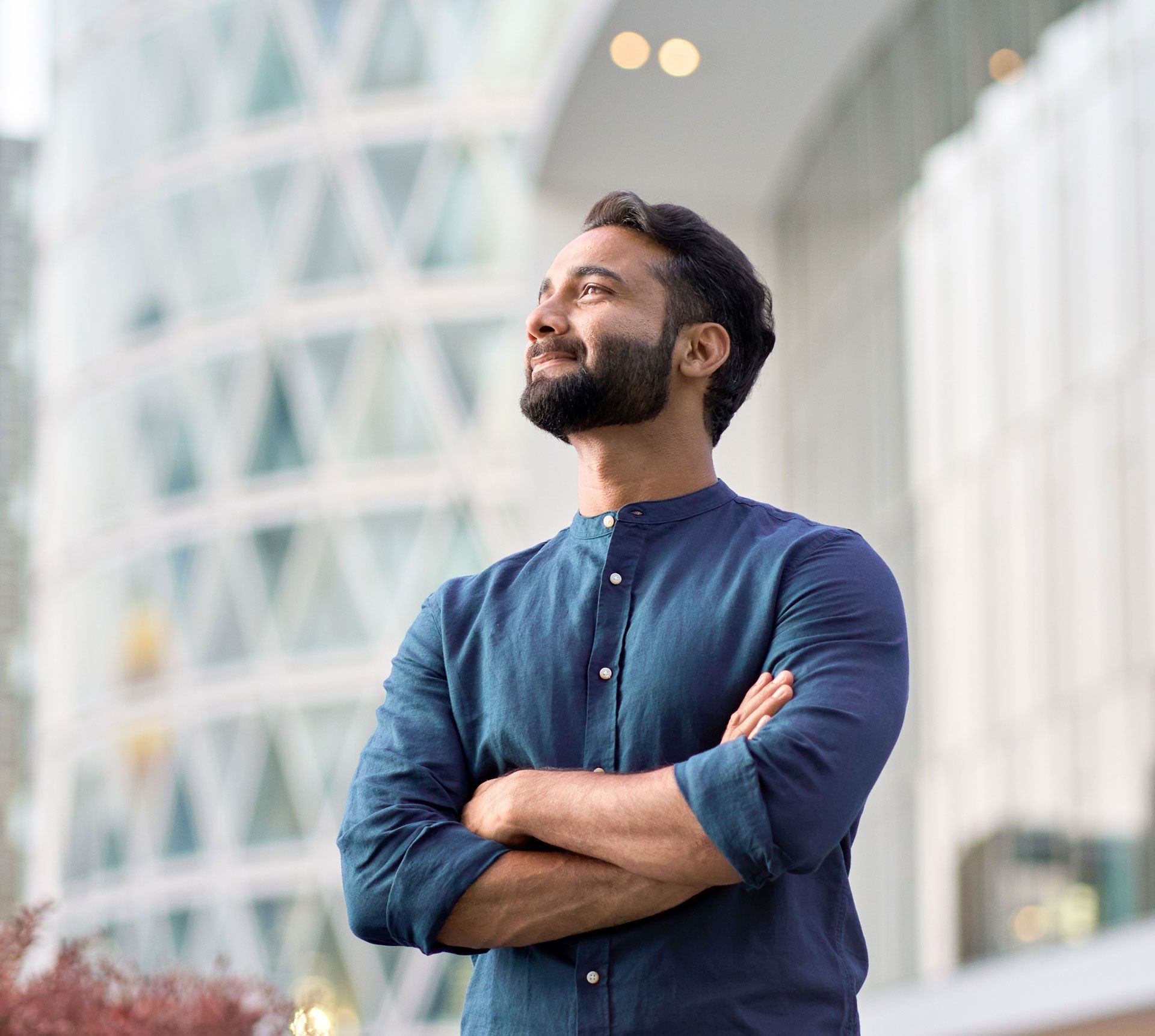 A man with a beard is standing in front of a building with his arms crossed.