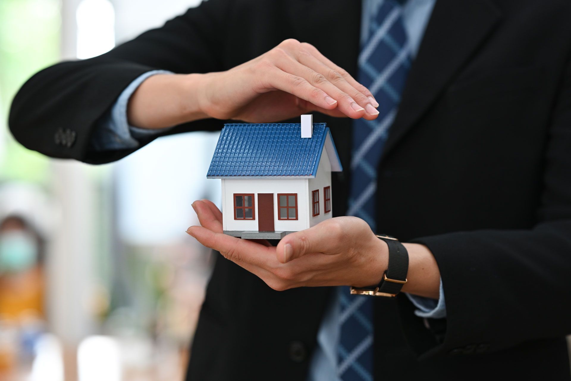 A man in a suit and tie is holding a model house in his hands.