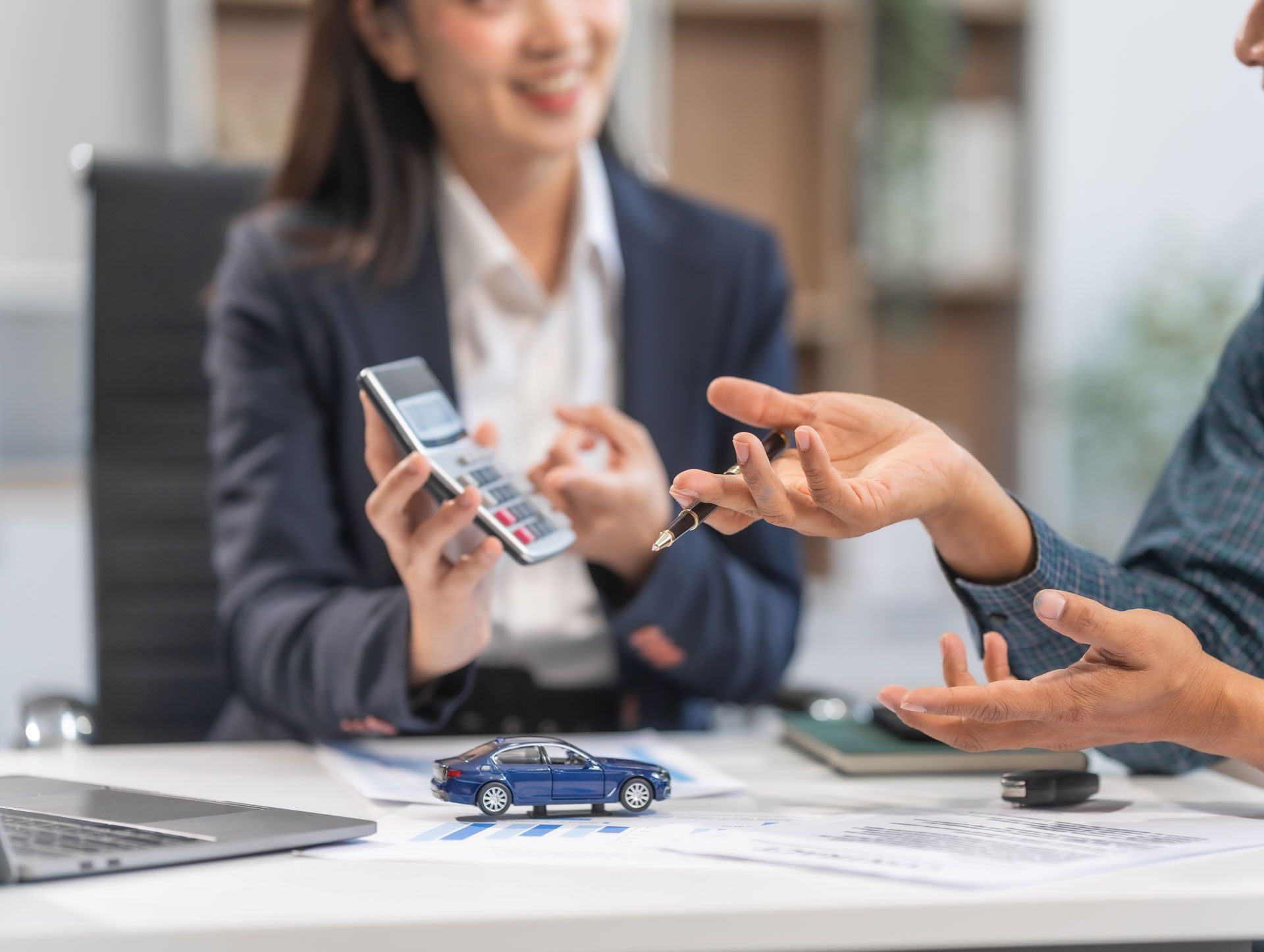 A woman is holding a calculator and a car key while a man gives her a car key.