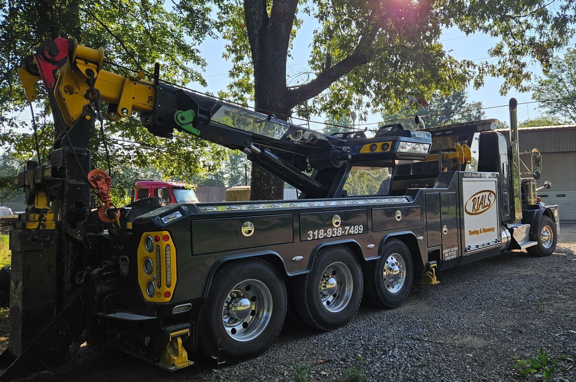 A tow truck with a crane attached to it is parked in front of a tree.