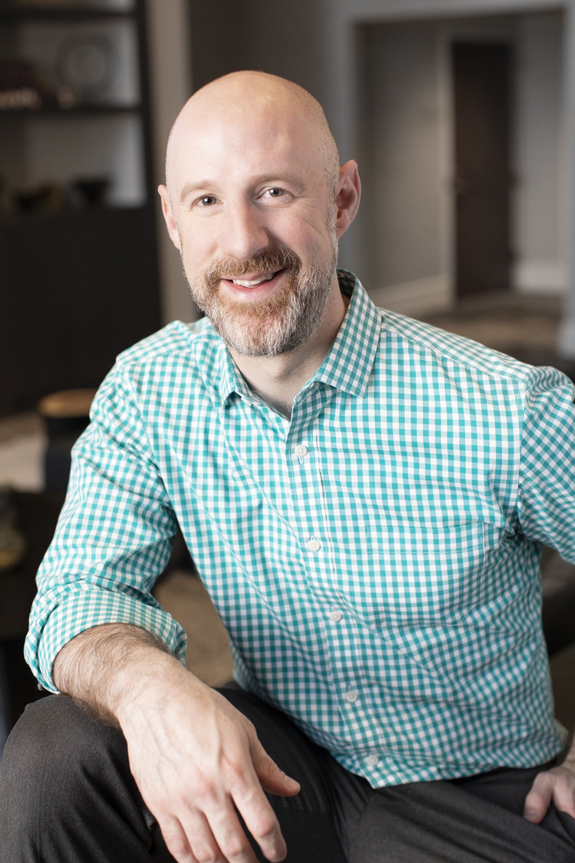 A bald man with a beard is wearing a green plaid shirt and smiling.