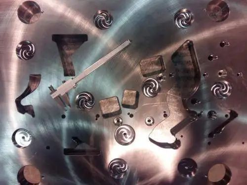 Piastra metallica con varie parti metalliche lavorate, pinze e motivi a spirale.