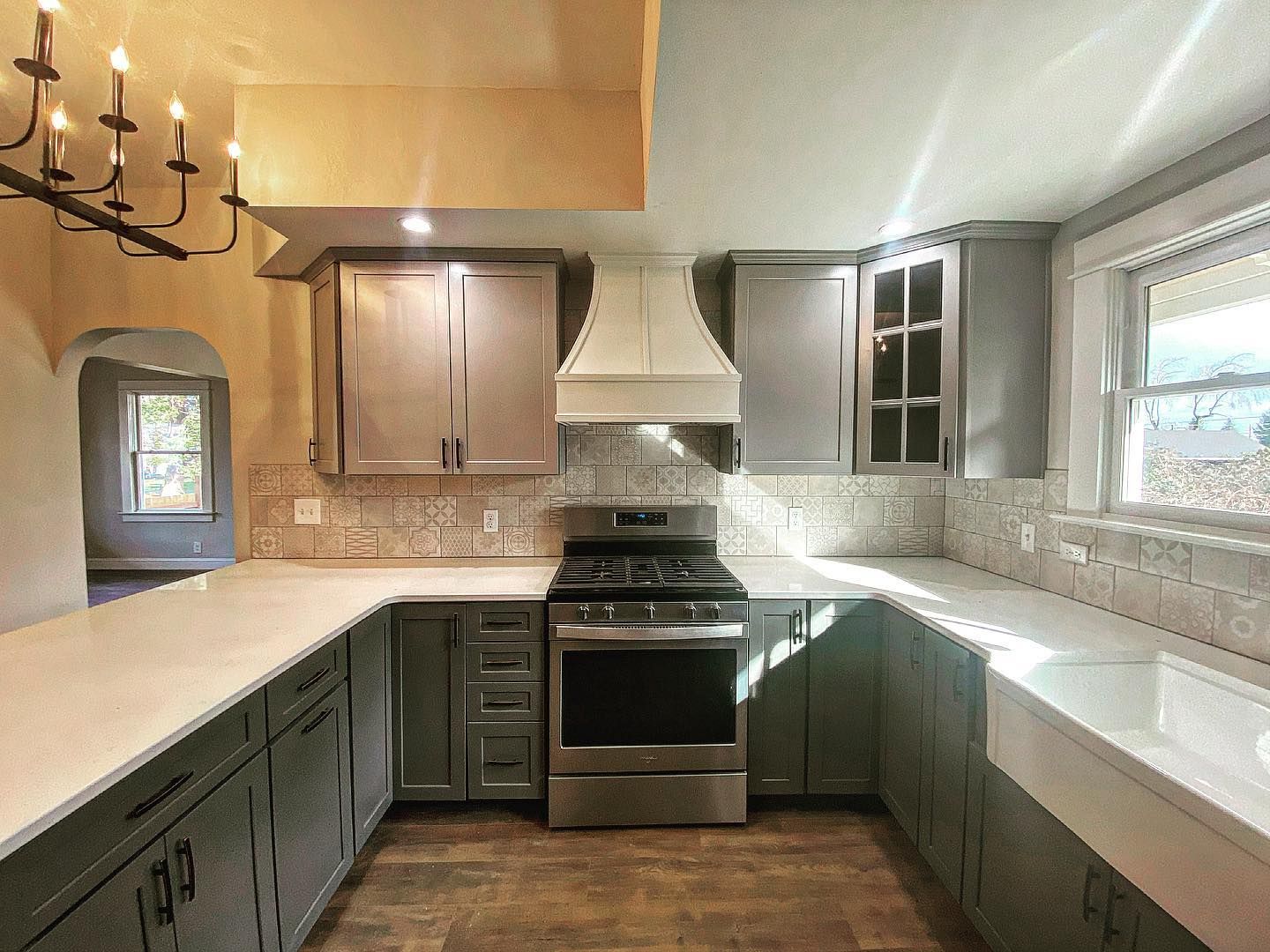 A mint-green kitchen with stone-tiled walls, dark countertops, upper glass-front cabinets, and a gas stove.