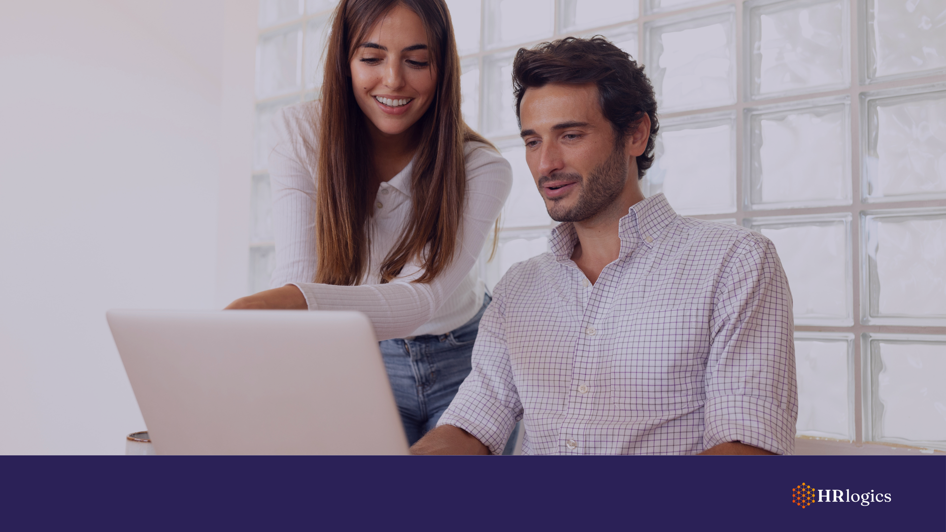 Two employees in a collaborative workspace viewing a digital employment verification on a laptop.