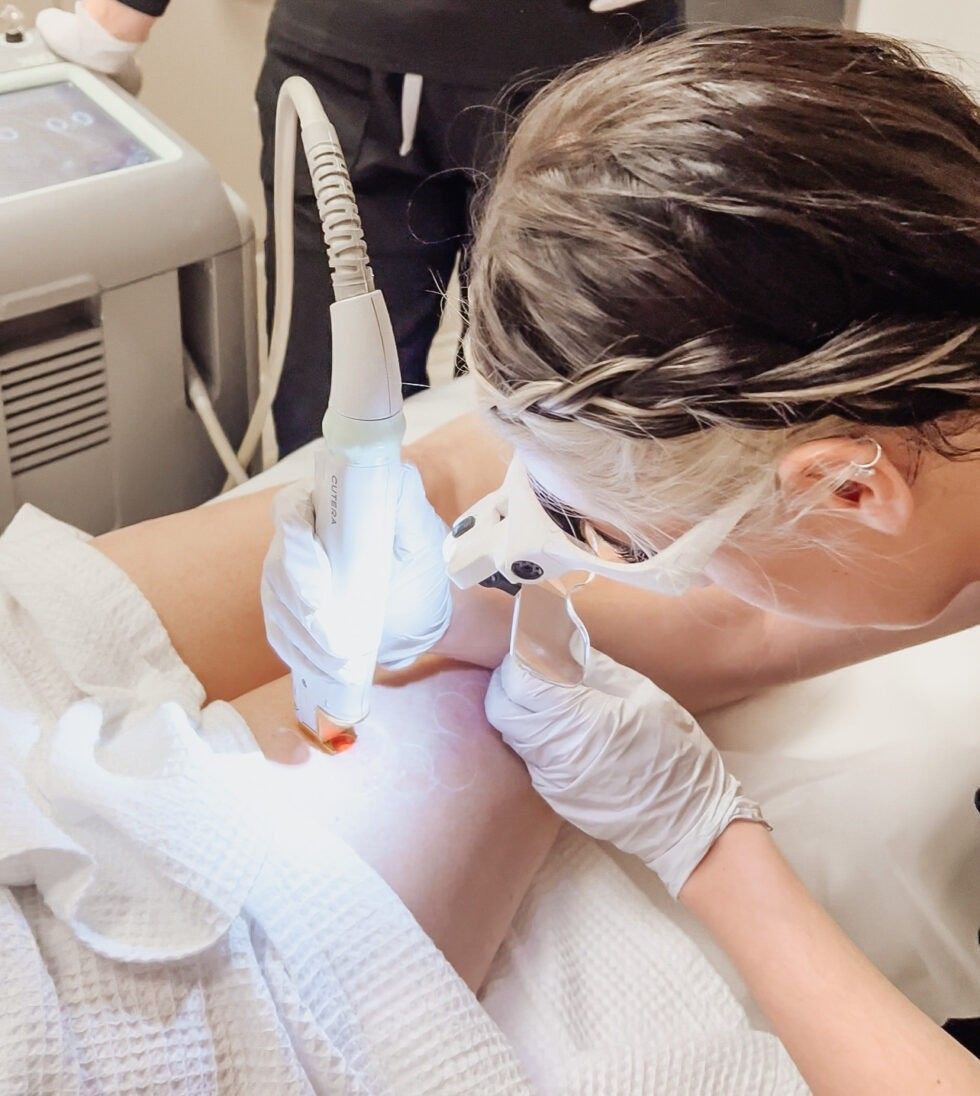 A woman wearing a mask and gloves is getting a laser treatment on her face.