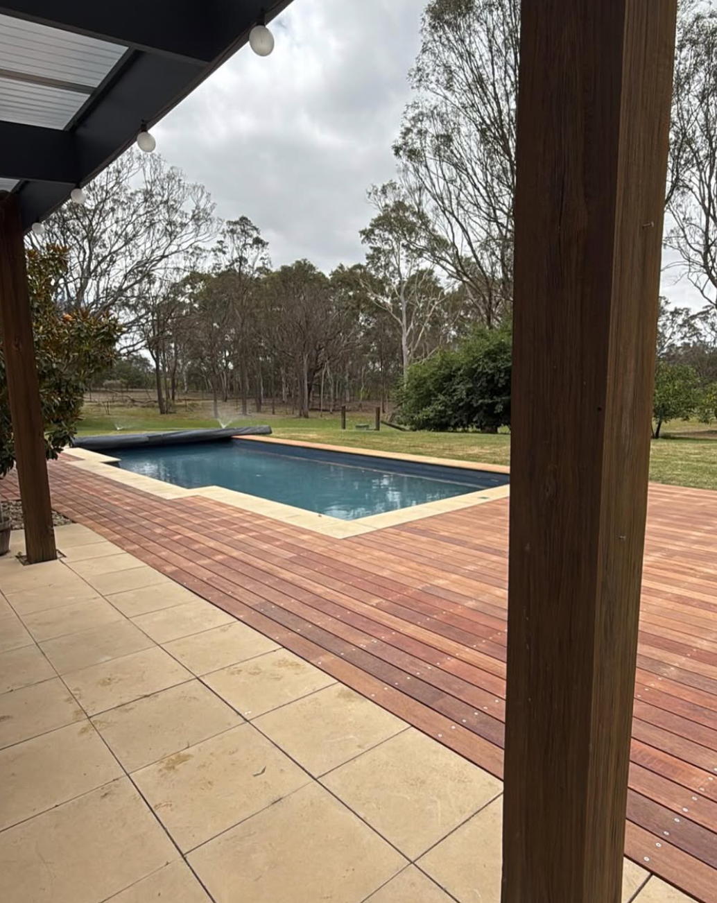 A large swimming pool is surrounded by trees and a wooden deck.