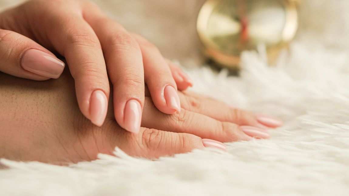 A close up of a woman 's hands with pink nails on a white blanket.