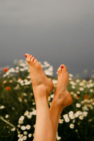 A woman 's feet are hanging over a field of daisies.