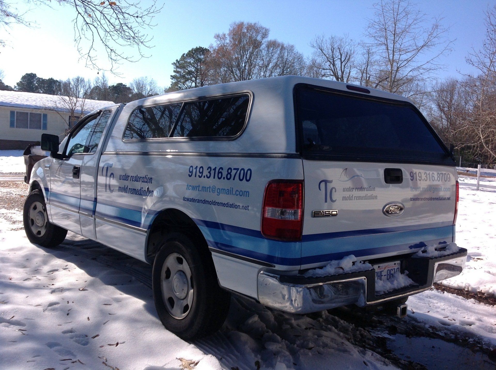 A white truck with a canopy is parked in the snow.