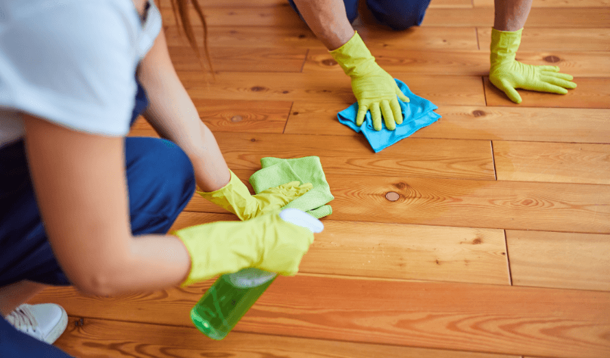 A man and a woman are cleaning a wooden floor.