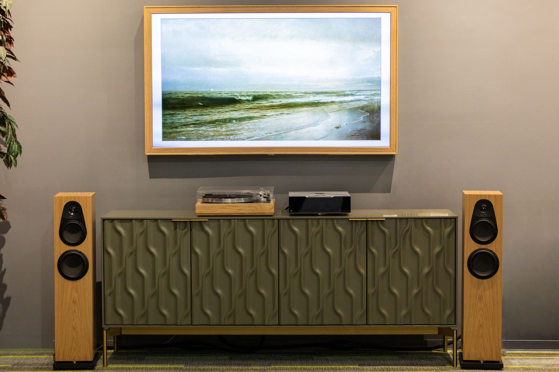Audio equipment on a console table beneath a seascape print. Tall wooden speakers flank the table.