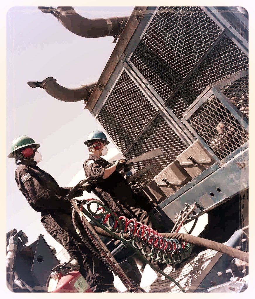 Two men wearing hard hats are working on a machine