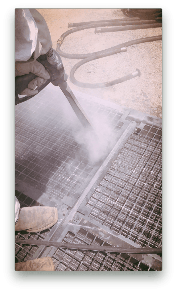 A person is sandblasting a metal surface with a machine.