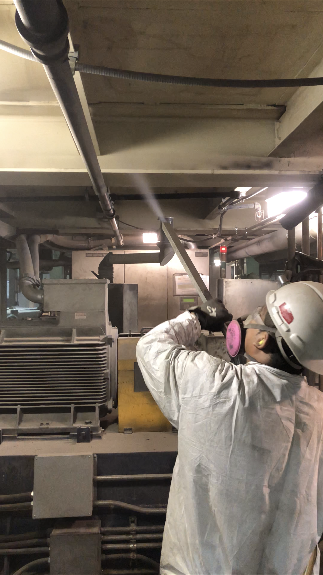 A man wearing a hard hat and ear muffs is working on a machine in a factory.