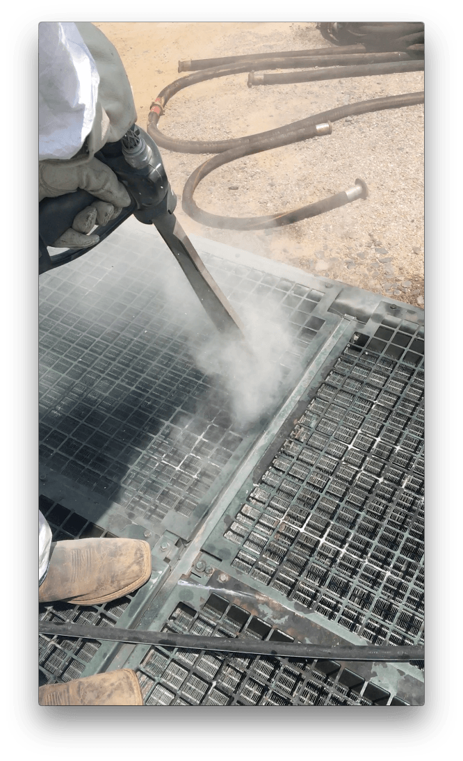 A person is using a high pressure washer to clean a metal grate.