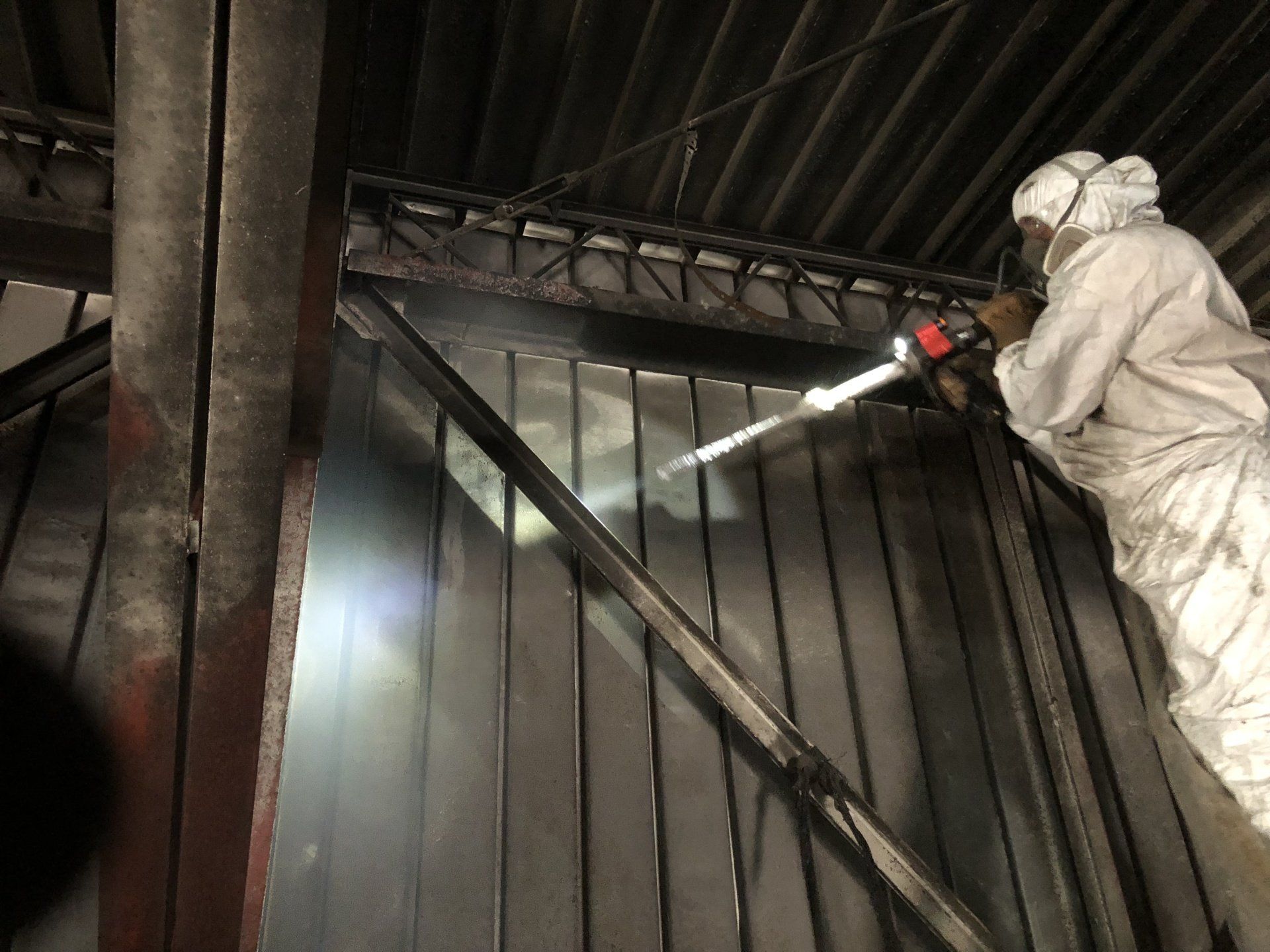 A man in a white suit is cleaning a wall with a high pressure washer.