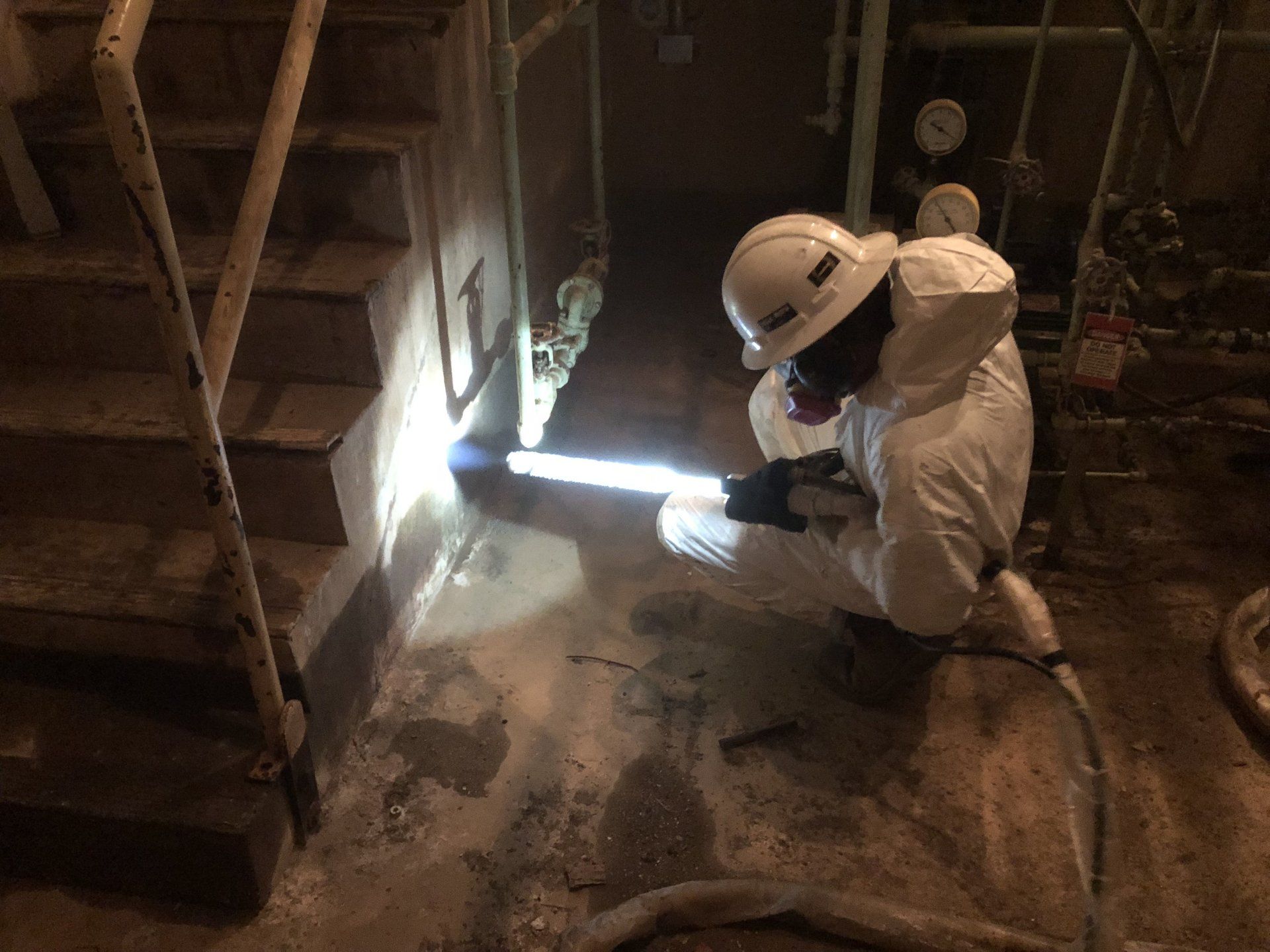 A man in a hard hat is kneeling down in a dark room.