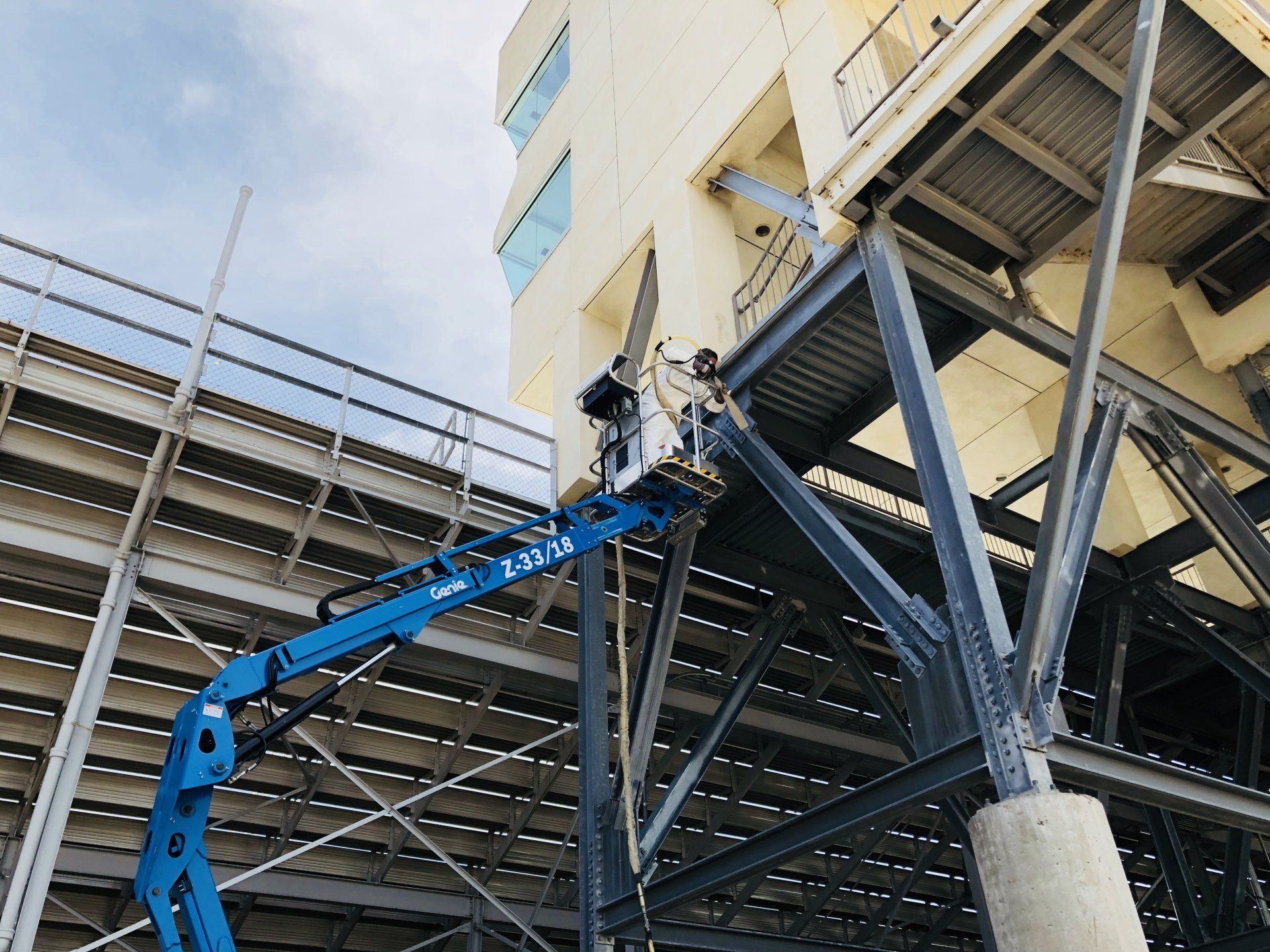 A man is standing on a crane in front of a building.